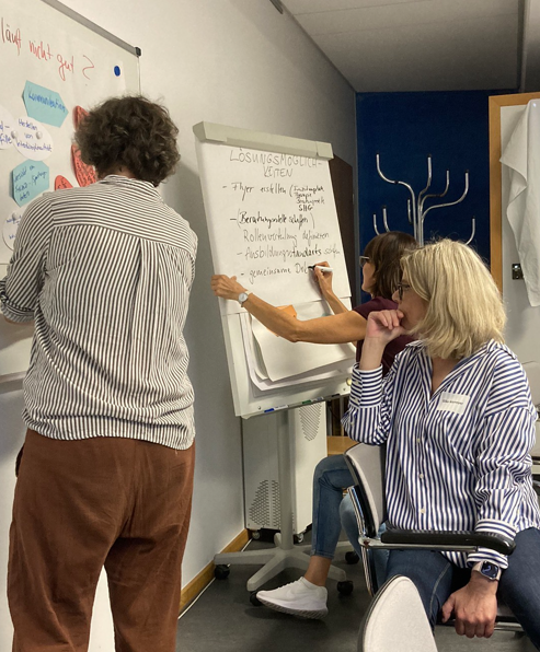Zwei Personen schreiben an einem Flipchart, eine schaut nachdenklich darauf 